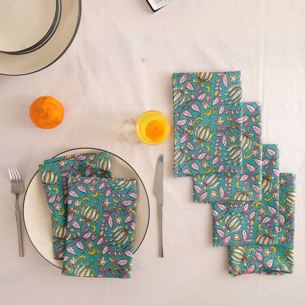 Set of four teal and pink block print cotton napkins fanned out on a laid table