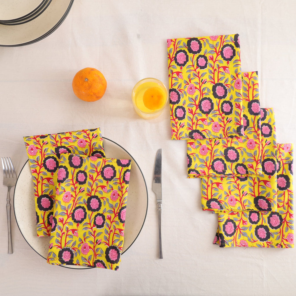 Set of four chartreuse and pink block print cotton napkins fanned out on a laid table