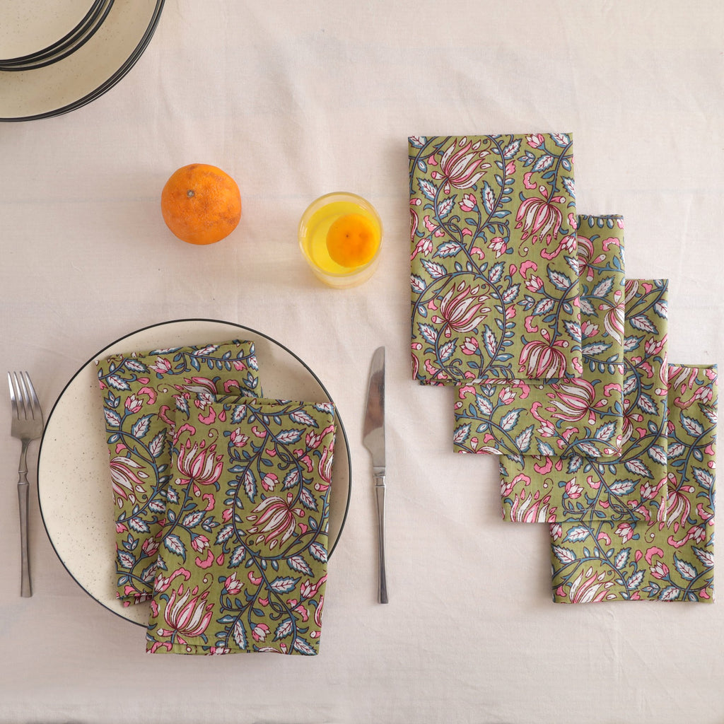 Set of four olive and pink block print cotton napkins fanned out on a laid table