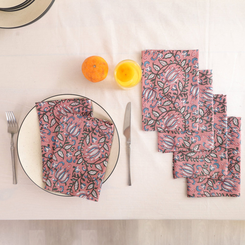 Set of four dusty rose block print cotton napkins fanned out on a laid table
