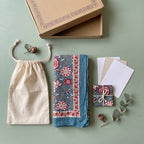 Slate and coral block print sarong folded with its cotton bag and packaging